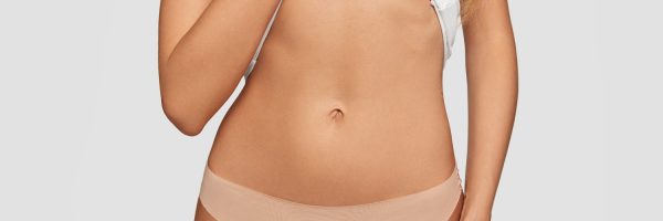 Cropped view of fit female shows her belly, has slim body, healthy pure skin, goes in for sport to stay fit, wears beige panties, isolated over white background. People, fitness and lifestyle concept