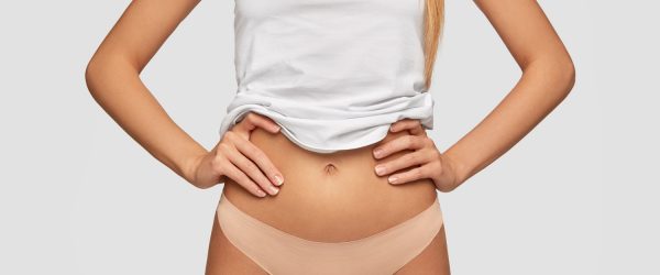 Cropped image of unrecognizable female with perfect slim body, keeps hands on waist, wears casual white top and panties, keeps to diet to be fit, isolated over white background. Fitness concept